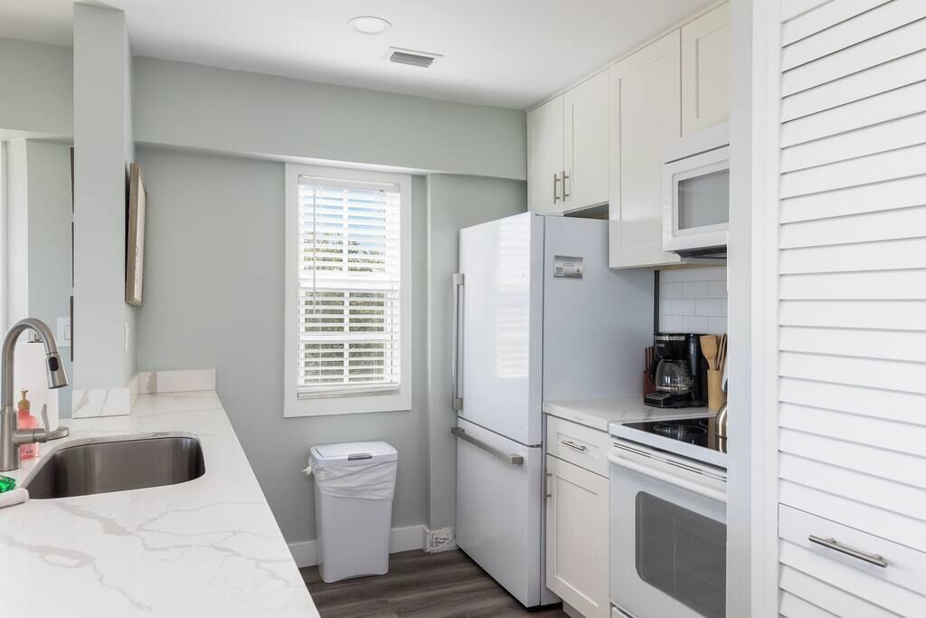 A kitchen with white cabinets, a stainless steel sink, a white refrigerator, and a microwave.