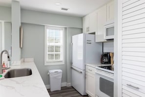 A kitchen with white cabinets, a stainless steel sink, a white refrigerator, and a microwave.