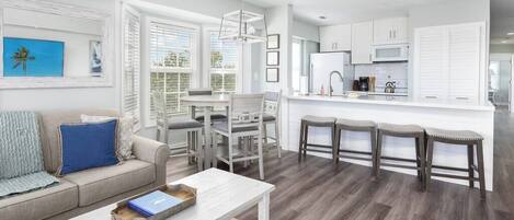Une cuisine moderne avec des meubles blancs, un îlot central doté de tabourets et un coin repas avec une table et des chaises blanches.