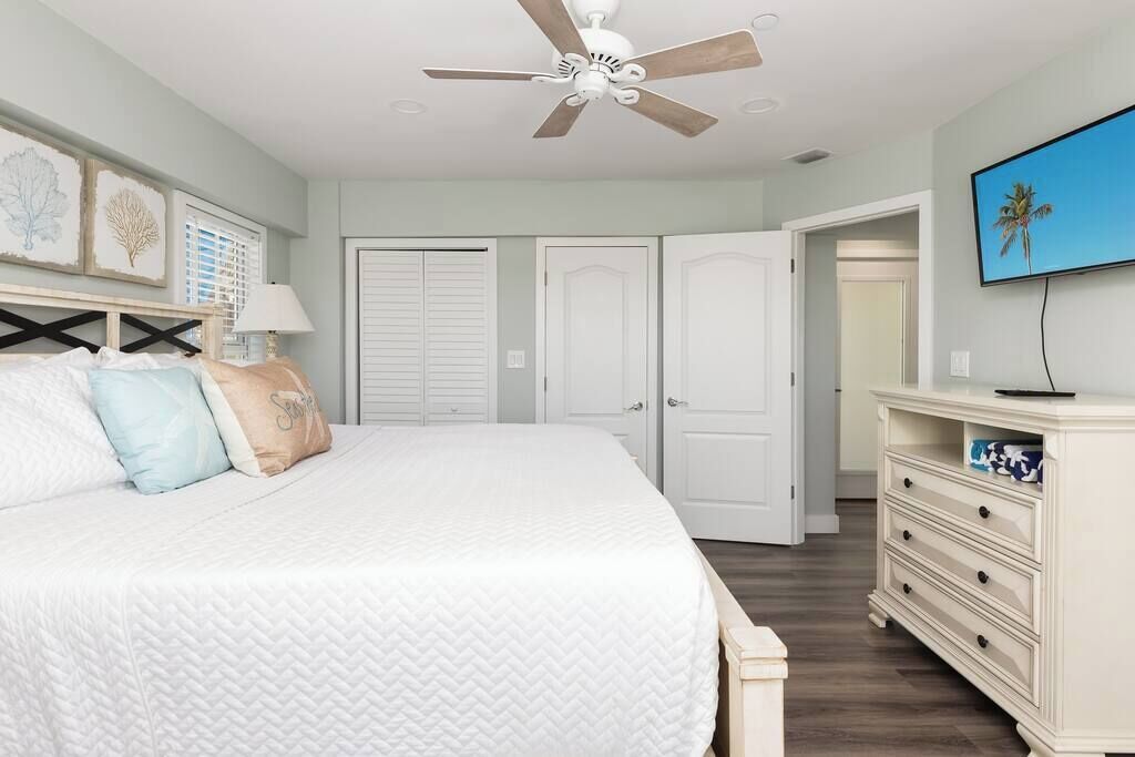 A bedroom with a bed, a ceiling fan, a TV, and a dresser.