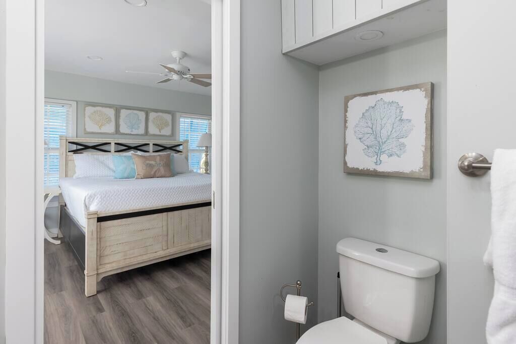 Ein Schlafzimmer mit einem Bett, einem Deckenventilator und einem Badezimmer mit Toilette sowie einem gerahmten Bild an der Wand.