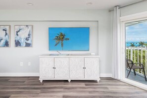 A room with a white cabinet, a painting of a palm tree, and a view of a balcony with a chair.