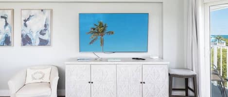 A room with a white cabinet, a white armchair, a small stool, and a painting of a palm tree.