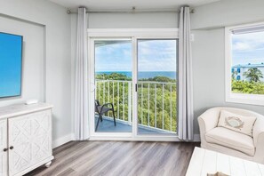 Una habitació amb un balcó, un sofà blanc i una televisió penjada a la paret.