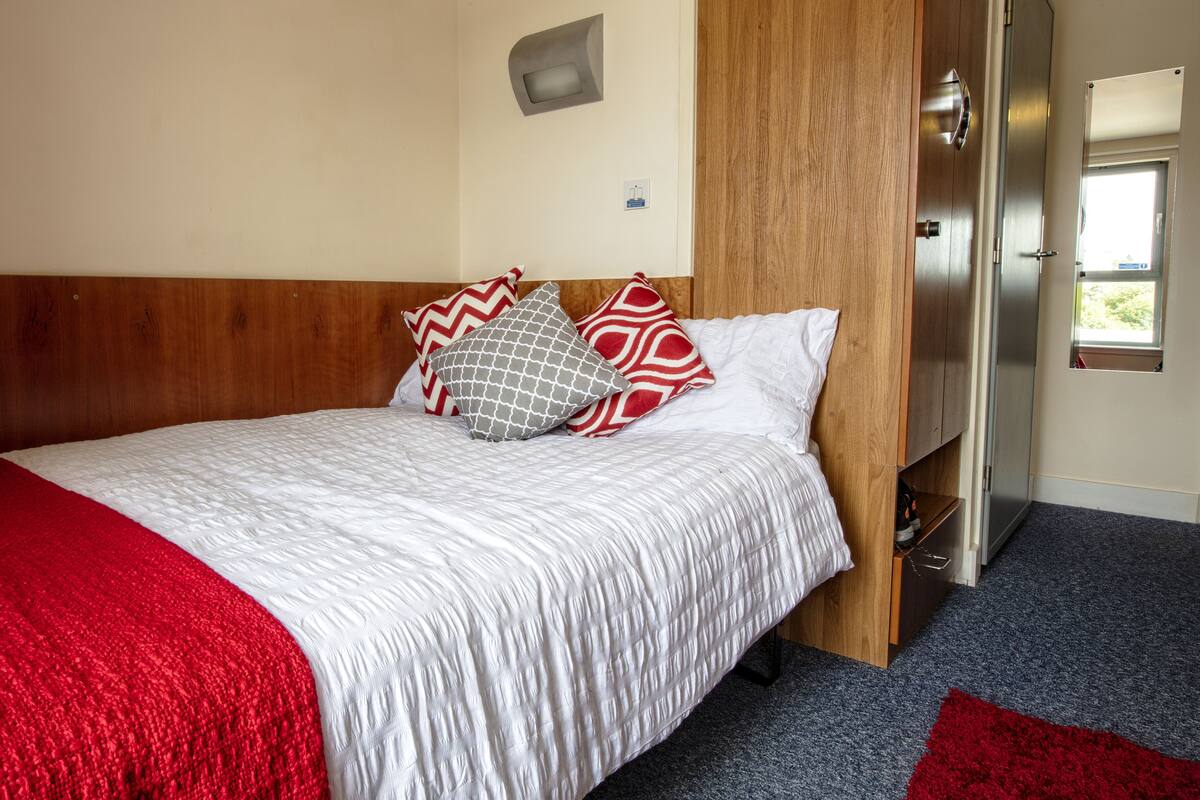 A neatly made bed with a red and white bedspread, two patterned pillows, and a wooden headboard.