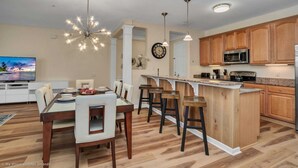 Une cuisine moderne avec des meubles en bois, un îlot central doté de tabourets de bar et un coin repas avec un téléviseur.