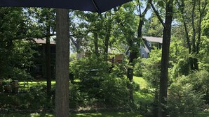 A patio area with a lounge chair and a table, surrounded by a stone wall and lush greenery. - Elegant Retreat in Montford Victorian! (Asheville)