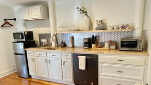 A modern kitchen with white cabinetry, a wooden countertop, a dishwasher, a microwave, a coffee maker, and a toaster. - Elegant Retreat in Montford Victorian! (Asheville)