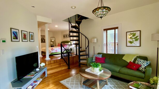 A living room with a green sofa, a coffee table, a TV, and a staircase leading to another room. - Elegant Retreat in Montford Victorian! (Asheville)