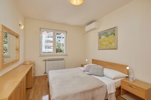 A bedroom with a bed, bedside table, lamp, and a window with a view of buildings.