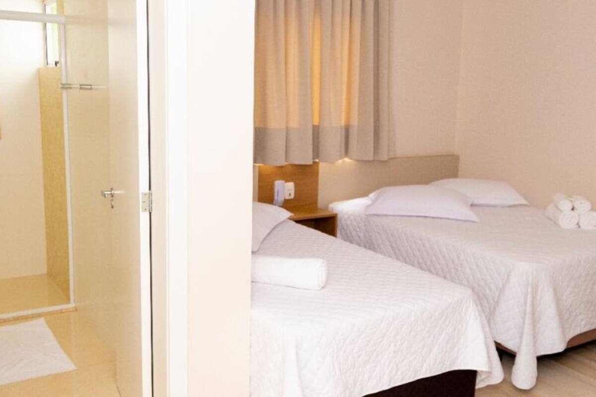A hotel room with two beds, a wooden headboard, a small bedside table, and a curtain.