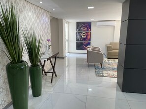 A modern lobby with a glass table, green vases, a beige sofa, and a large abstract painting. - Hotel Serrano (Frederico Westphalen)