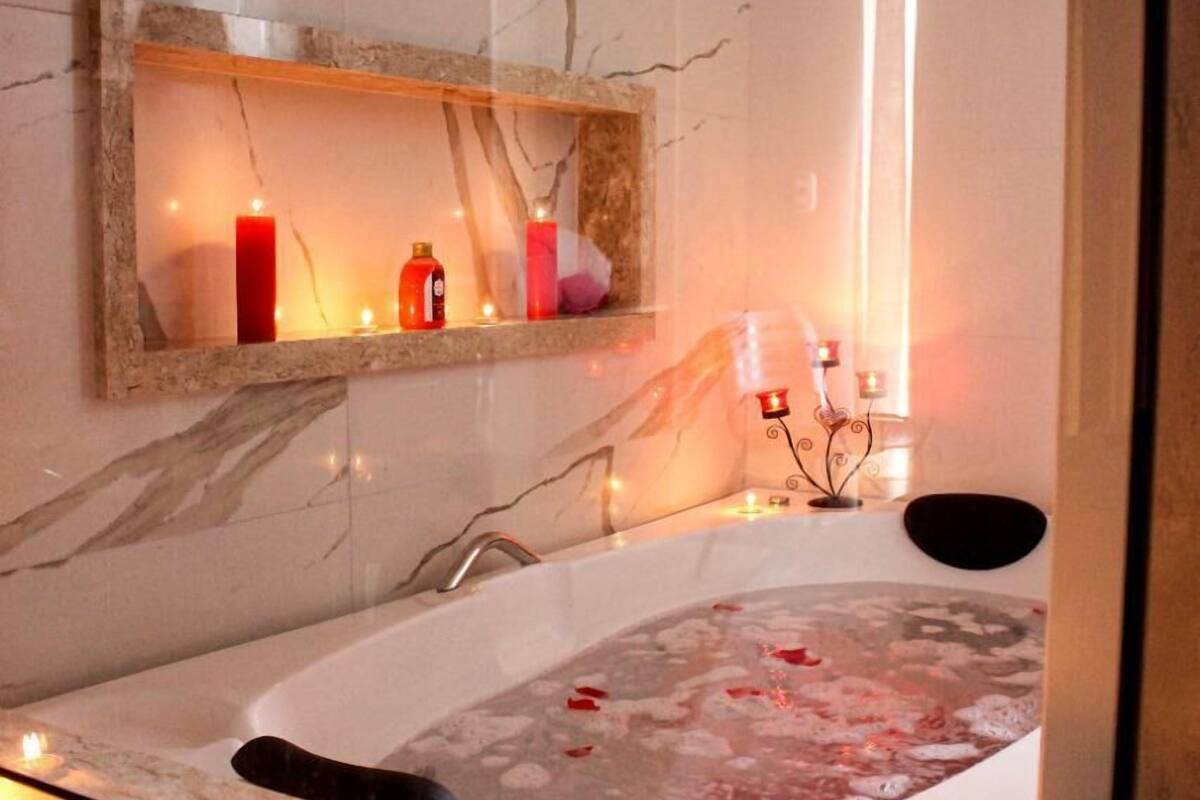 A bathroom with a marble wall, a bathtub with candles, and a shelf with toiletries.