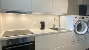 A modern kitchen with white cabinets, a built-in oven, a coffee machine, and a washing machine. - Newly renovated basement apartment with nice view (Møre og Romsdal)