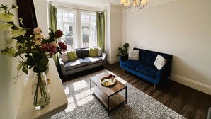 Un salon avec un canapé gris, un canapé bleu, une table basse et un lustre.
