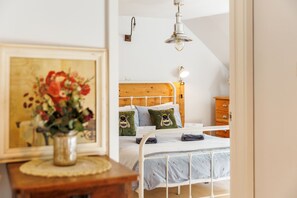 A bedroom with a wooden headboard, a white metal bed frame, a bedside table with a vase of flowers, and a wooden dresser. - 1 Apse Castle Cottage (Shanklin)