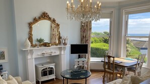 Ein Wohnzimmer mit einer Chandelüster, einem Kamin, einem Fernseher und Meerblick.