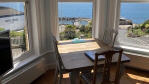 Ein Zimmer mit großem Fenster und Meerblick, einem Holztisch und einem Stuhl.