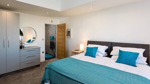 A modern hotel room with a large bed, a bedside table with a lamp, a wardrobe, and a bathroom with a shower. - New Horizon (Sandown)