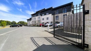 A gated parking area with multiple cars parked in front of a modern building with multiple windows. - New Horizon (Sandown)