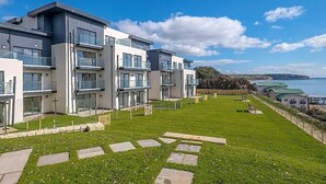 A modern apartment complex with multiple balconies, a grassy lawn, and a view of the sea. - New Horizon (Sandown)