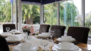 A dining table set with white plates, gold chargers, and wine glasses, overlooking a tropical garden with palm trees. - No 1 Ashey (Ryde)