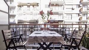 Ein Balkon mit Tisch für zwei Personen, umgeben von Holzstühlen und einer Blumenvase.