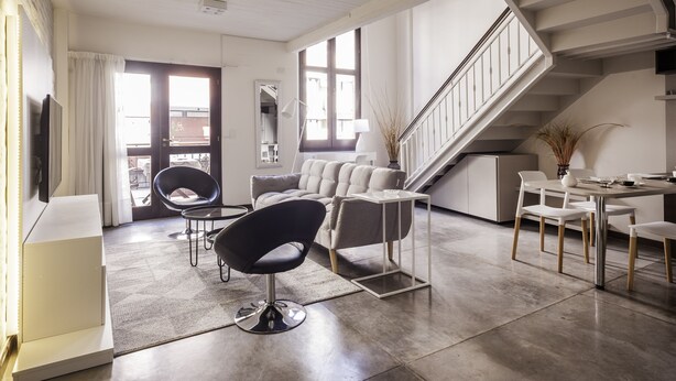 Ein modernes Wohnzimmer mit einer Couch, Sesseln, einem Couchtisch, einem Fernseher und einer Treppe.