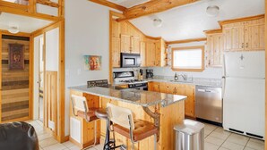 A kitchen with wooden cabinets, a granite countertop, a stainless steel refrigerator, and a dishwasher. - The Zen Den (Cedar City)