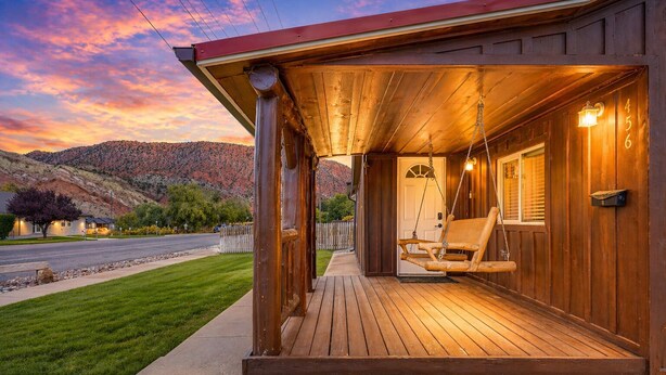 A wooden cabin with a porch, a swing, and a door with a number. - The Zen Den (Cedar City)