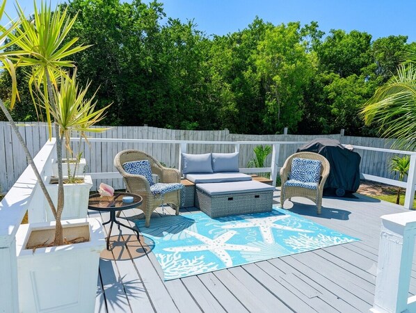 Una terraza con mobiliario de mimbre, un tapete con estampado de estrella de mar azul y una cerca blanca.