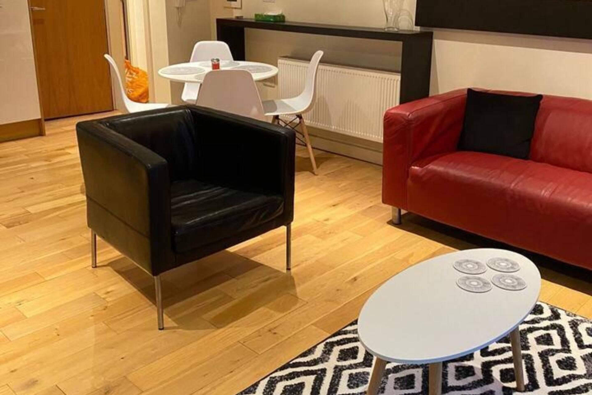 A modern living room with a black leather armchair, a red leather sofa, a white round coffee table, and a patterned rug.
