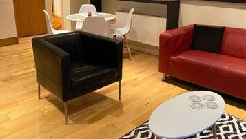 A modern living room with a black leather armchair, a red leather sofa, a white round coffee table, and a patterned rug.