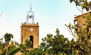 A stone clock tower with a weather vane, surrounded by greenery. - Le Mimosa apartment with private terrace on garden level, a stone's throw from the village. (Le Plan-de-la-Tour)