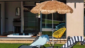 Une villa moderne dotée d’une piscine, de chaises longues et d’un parasol en chaume.