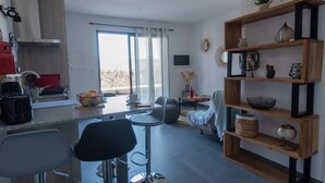 Une cuisine moderne avec un coin repas, un tabouret de bar et une étagère en bois agrémentée d’objets décoratifs.
