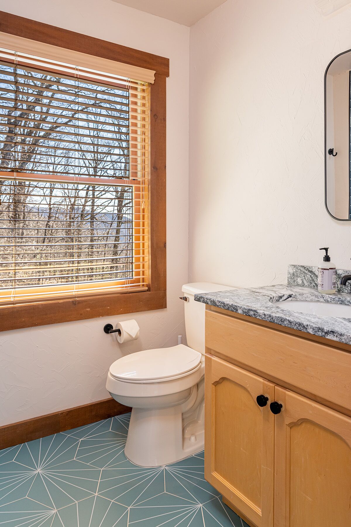 Une salle de bain comprenant des toilettes, un lavabo avec un plan de toilette en marbre et une fenêtre avec des stores.
