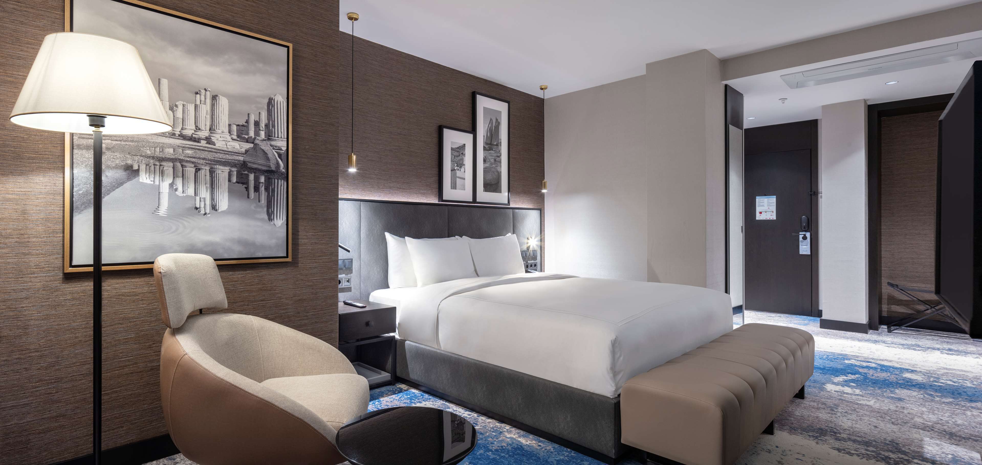 Una habitación de hotel moderna con una cama grande, una silla, un escritorio y una lámpara de pared.