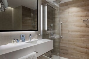 Un baño moderno con un espejo grande, un lavabo blanco y una cabina de ducha con mampara de vidrio.
