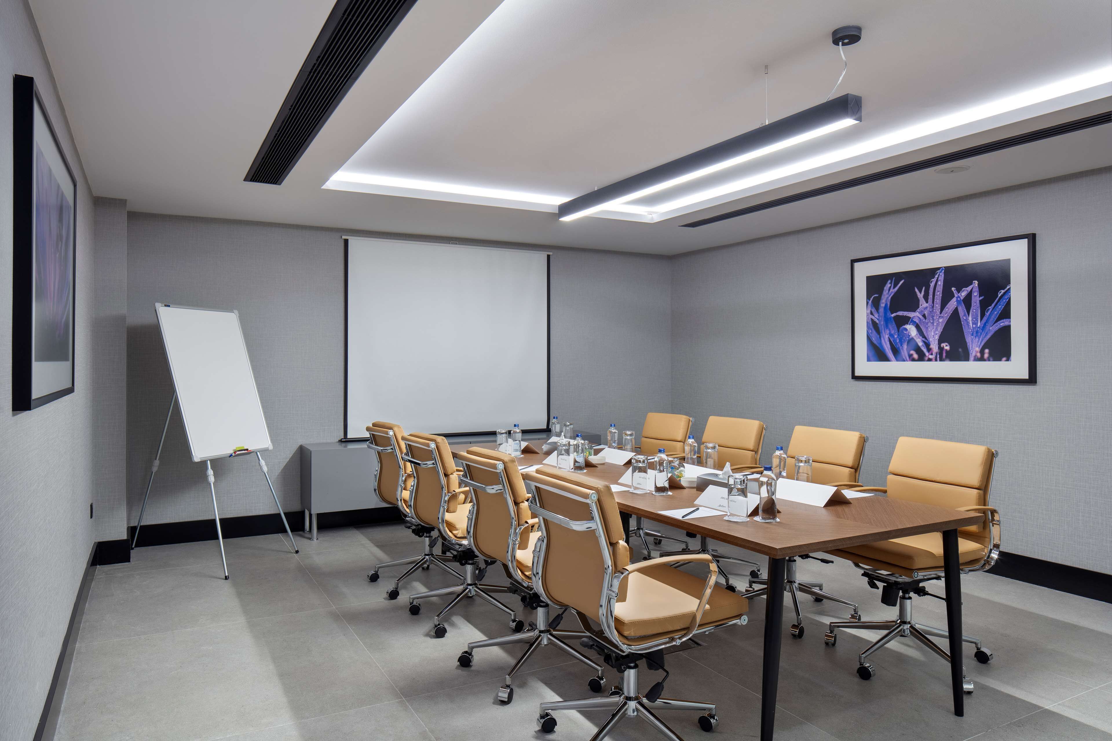 A conference room with a long table, six chairs, a whiteboard, and a projector screen.