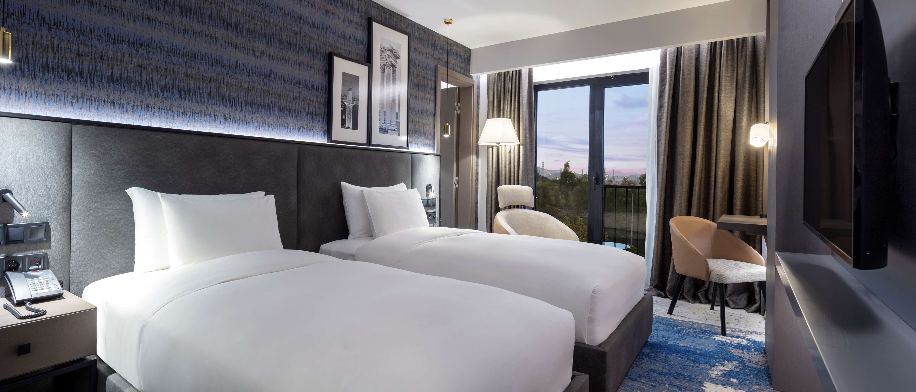 A hotel room with two beds, a desk, a chair, a TV, and a phone on the nightstand.
