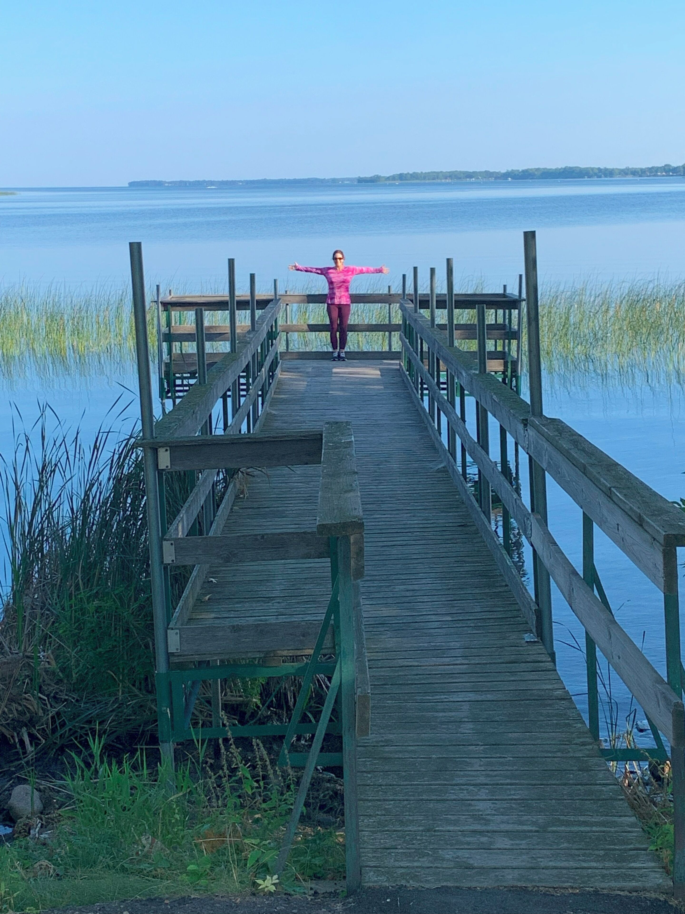 A wooden pier extending into calm water with a person standing at the end.