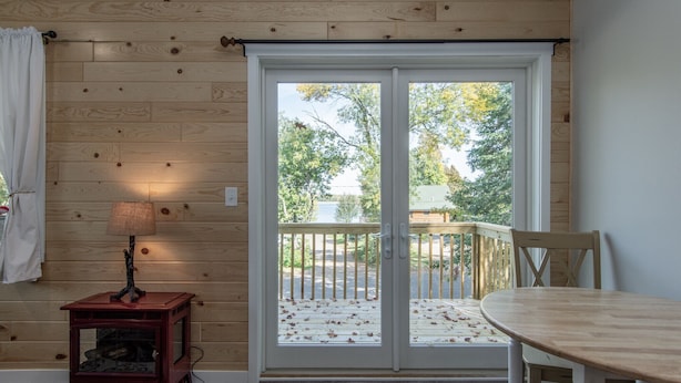 A room with a wooden floor, a table, a chair, a lamp, and a sliding glass door leading to an outdoor deck. - Conveniently located New Cabin at Lake Mille Lacs  (Isle)