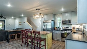 A modern kitchen with a central island, wooden chairs, a built-in stove, and stainless steel appliances. - Conveniently located New Cabin at Lake Mille Lacs  (Isle)