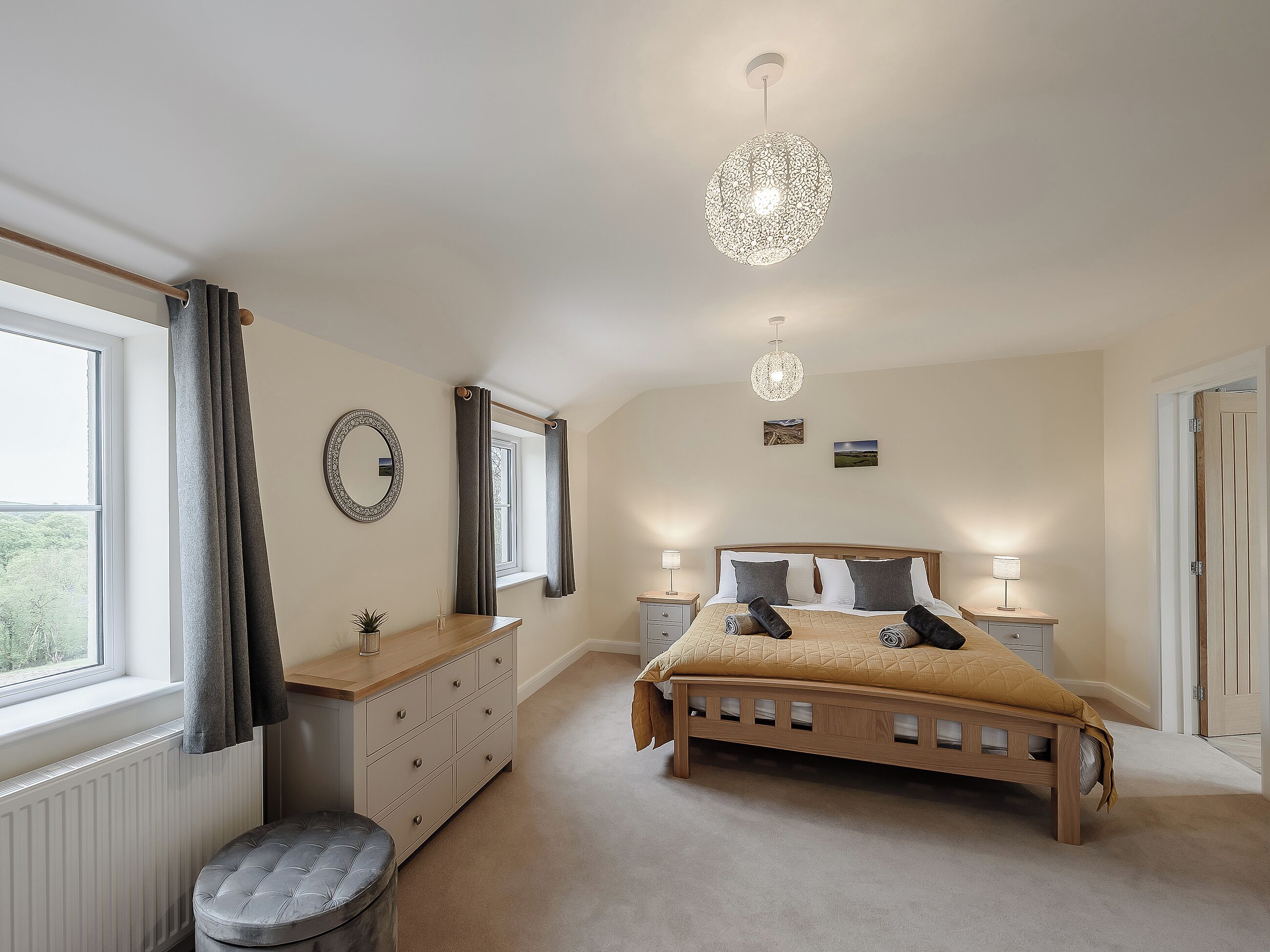 A bedroom with a bed, bedside tables, a dresser, a window with curtains, and a hanging light fixture.