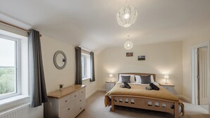 Une chambre à coucher comprenant un lit, des tables de chevet, une commode, une fenêtre avec des rideaux et un luminaire suspendu.
