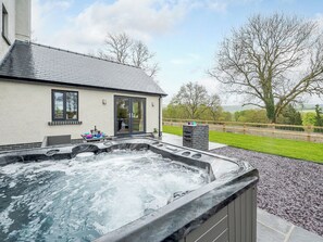Un área de spa con un jacuzzi, una pequeña mesa con objetos y vistas a una casa y el paisaje.