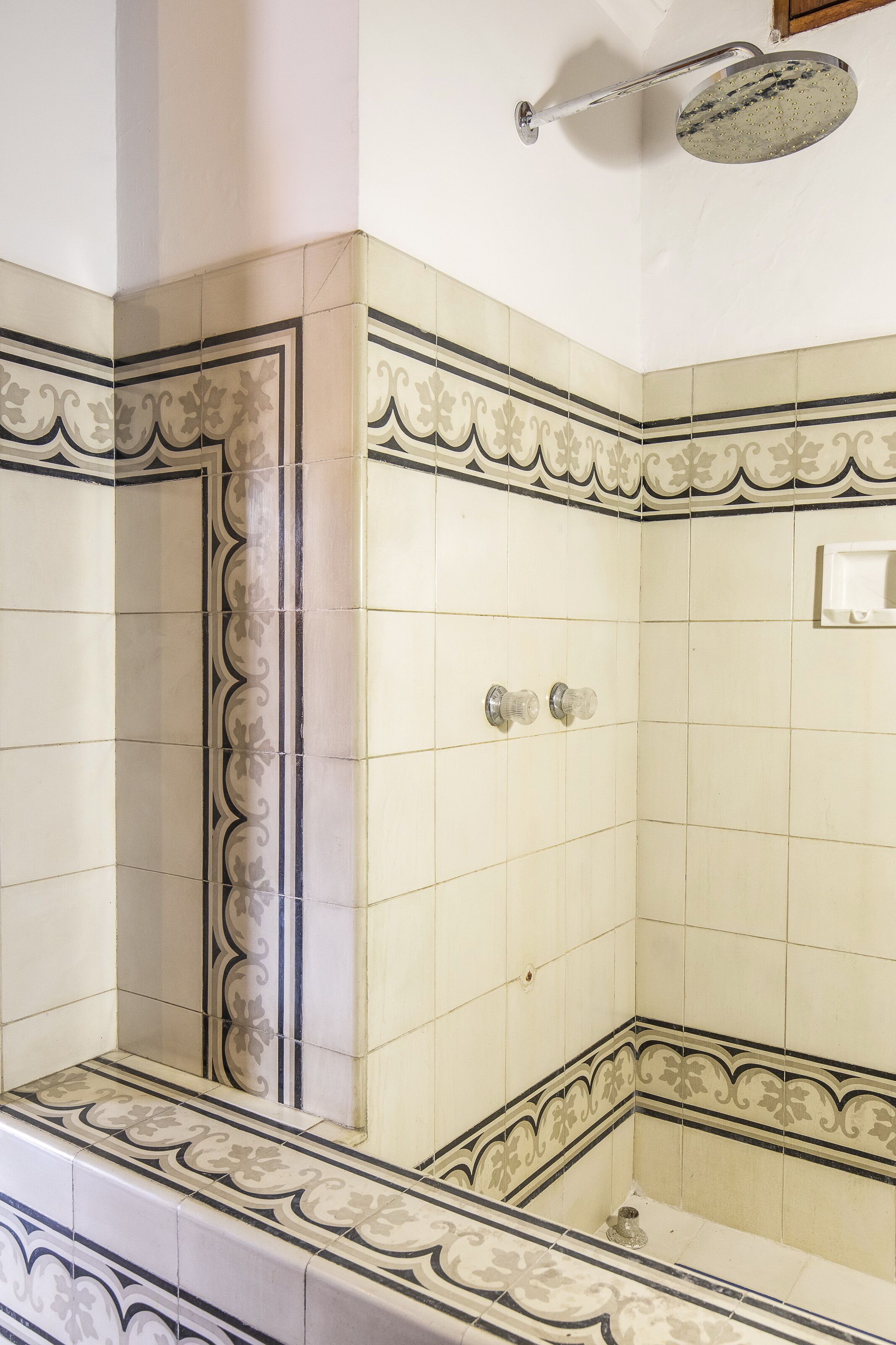 Esquina de un baño con azulejos decorativos, ducha y lavamanos pequeño.