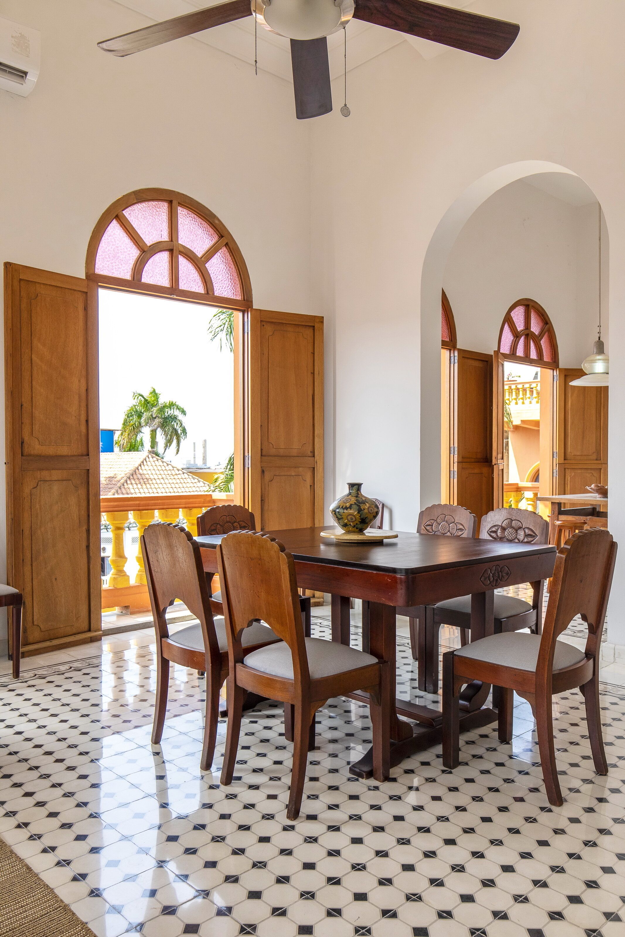 Un'area pranzo con un tavolo e sedie in legno, un vaso decorativo e vista all'esterno attraverso una porta aperta.