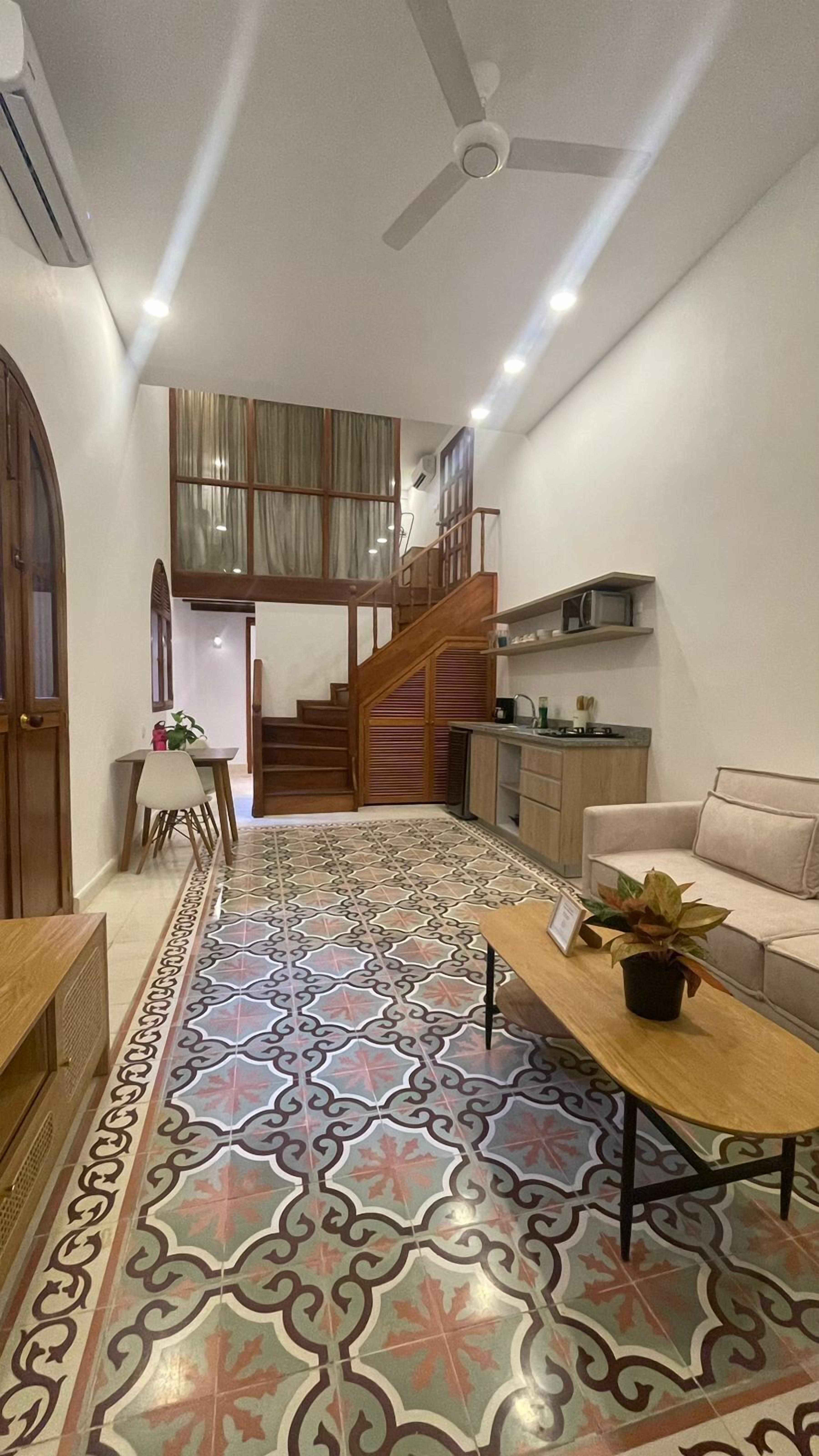 A spacious living area with a patterned floor, a staircase to an upper level, a kitchen area, and a seating area with a plant.